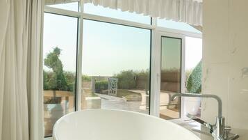 A modern bathroom with a large oval bathtub, a chandelier, and a view of the outdoors through large windows.