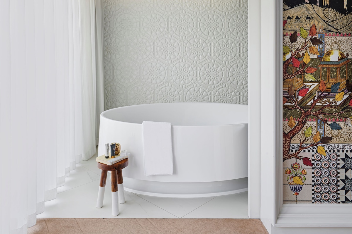 A modern bathroom with a freestanding bathtub, a chandelier, and a decorative wall with a geometric pattern.