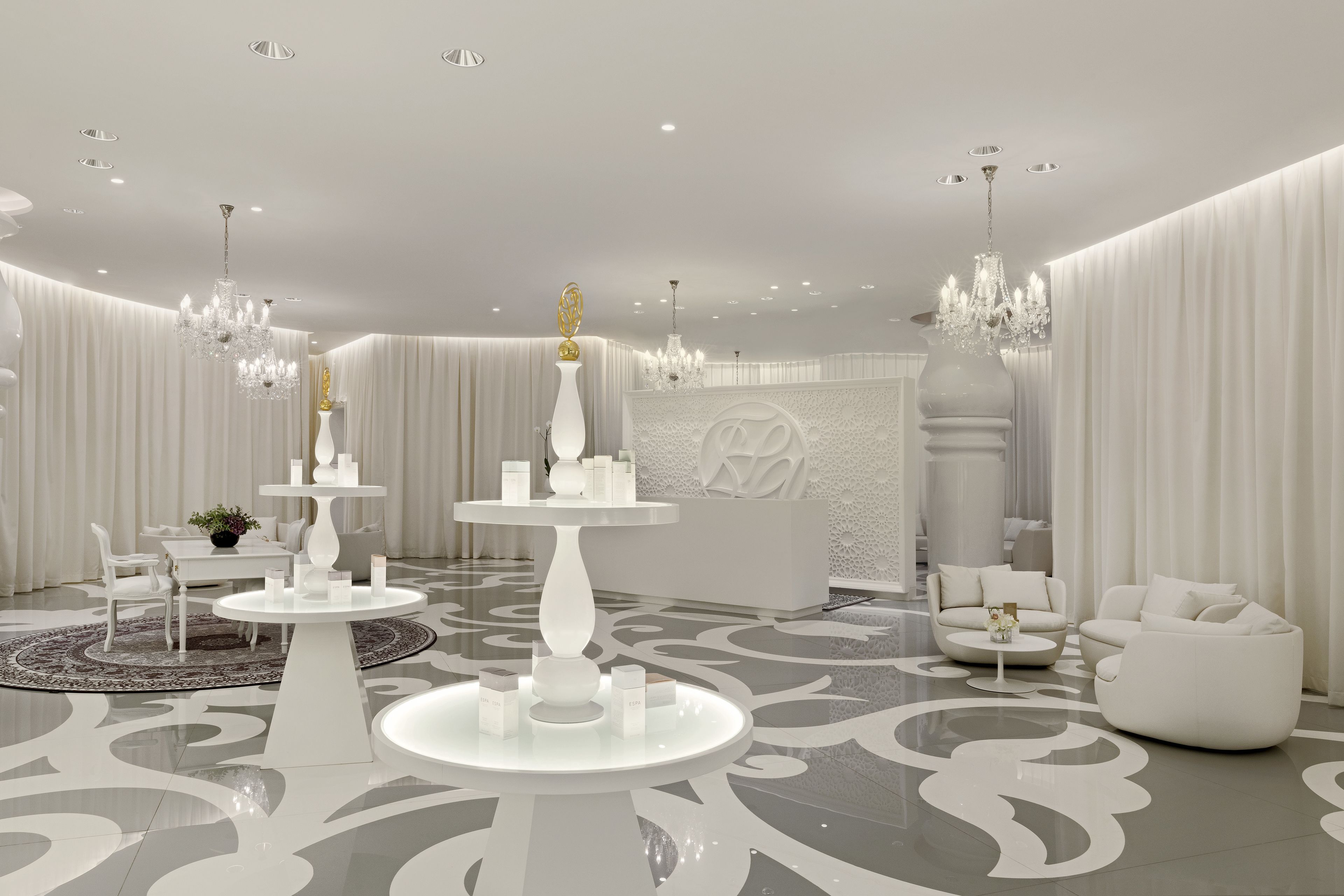 A modern, elegantly designed room with a central white table, a chandelier, and a sofa.