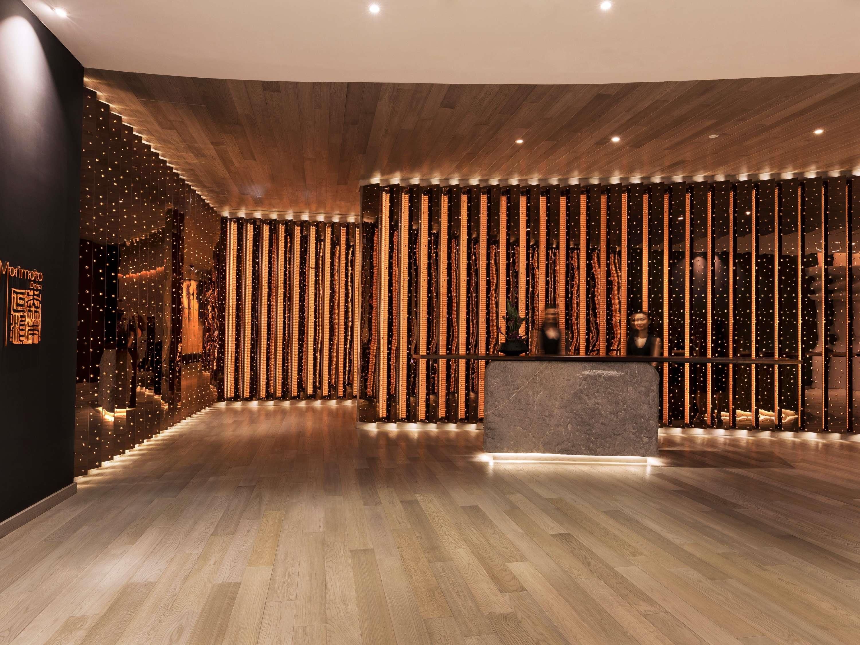 Un vestíbulo moderno de hotel con suelo de madera, una recepción y lámparas verticales.