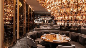 Un bar lujoso con una mesa redonda rodeada de sofás, elegantes lámparas colgantes y una amplia selección de vinos.