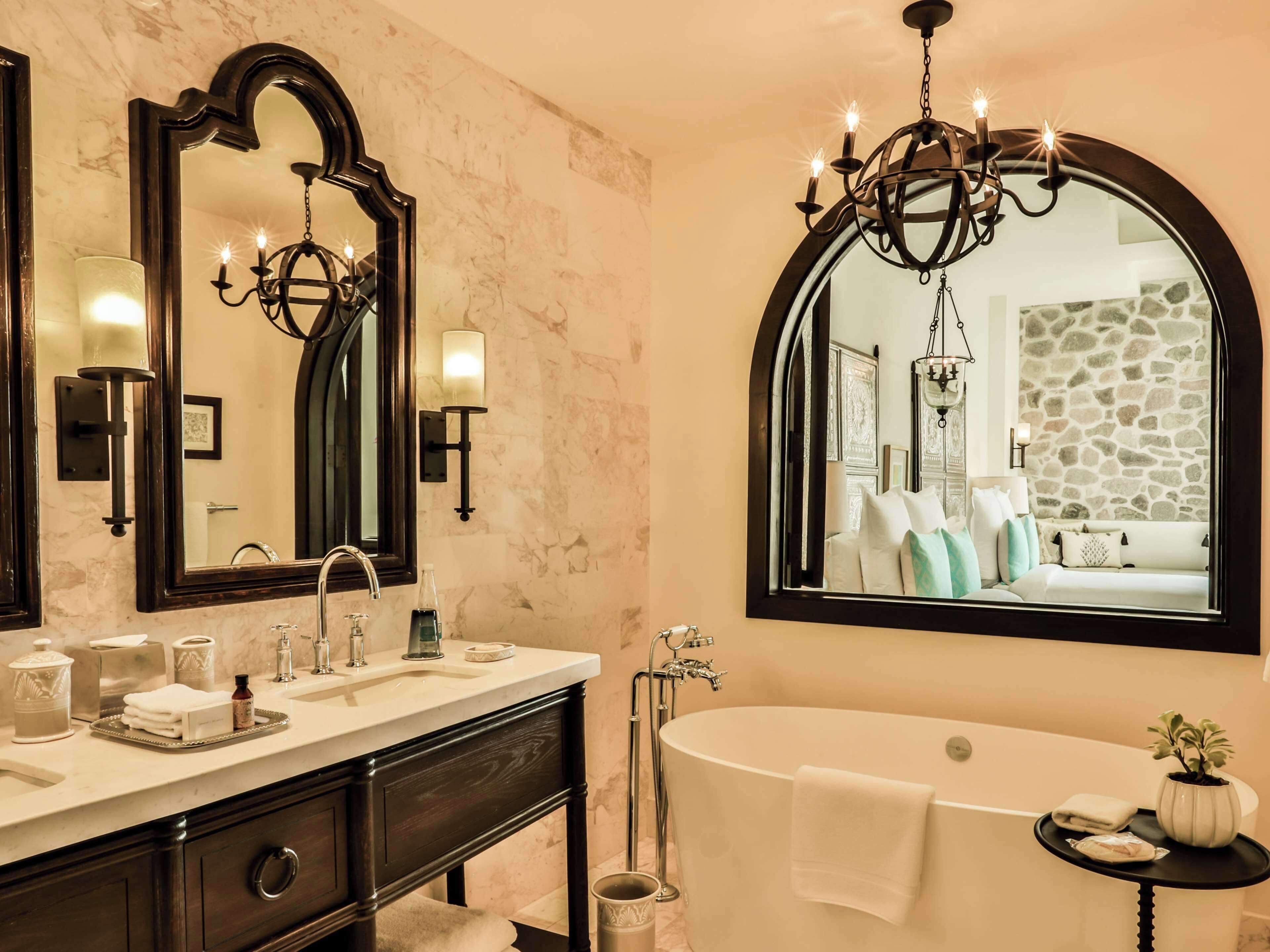 A bathroom with a double sink, a large mirror, a chandelier, and a bathtub.