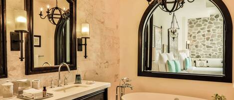 A bathroom with a double sink, a large mirror, a chandelier, and a bathtub.