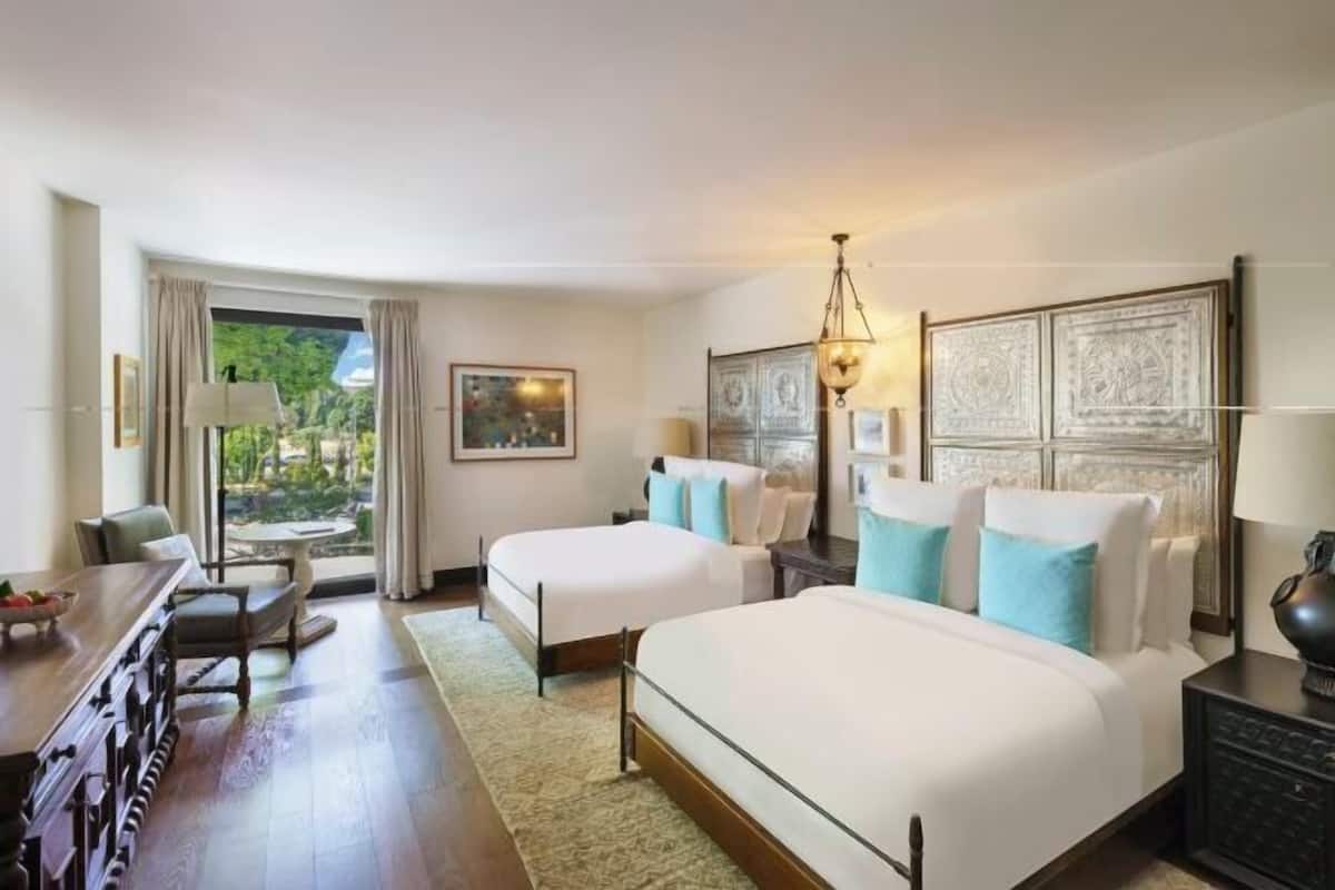 A hotel room with two beds, a dining table, a desk, and a view of the outdoors.