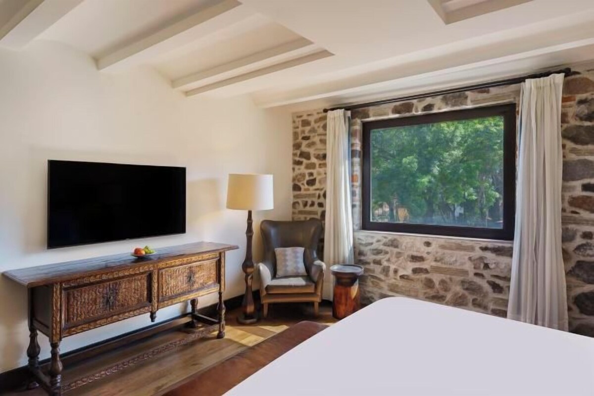 Un dormitorio con un ventanal grande, un televisor de pantalla plana, un mueble de madera y una silla.