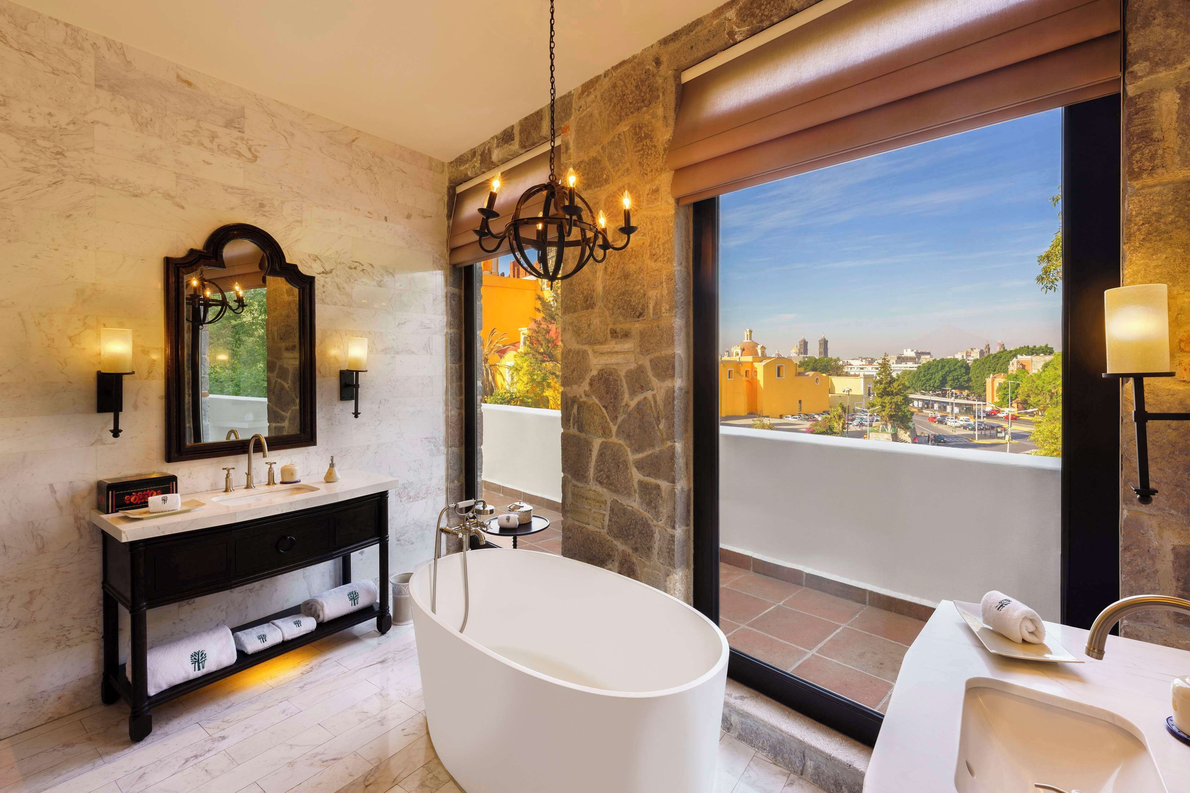 A modern bathroom with a freestanding bathtub, a vanity with a mirror, and a view of the city through large windows.