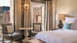 Una habitación de hotel con una cama, dos sillones, una mesita y una lámpara.