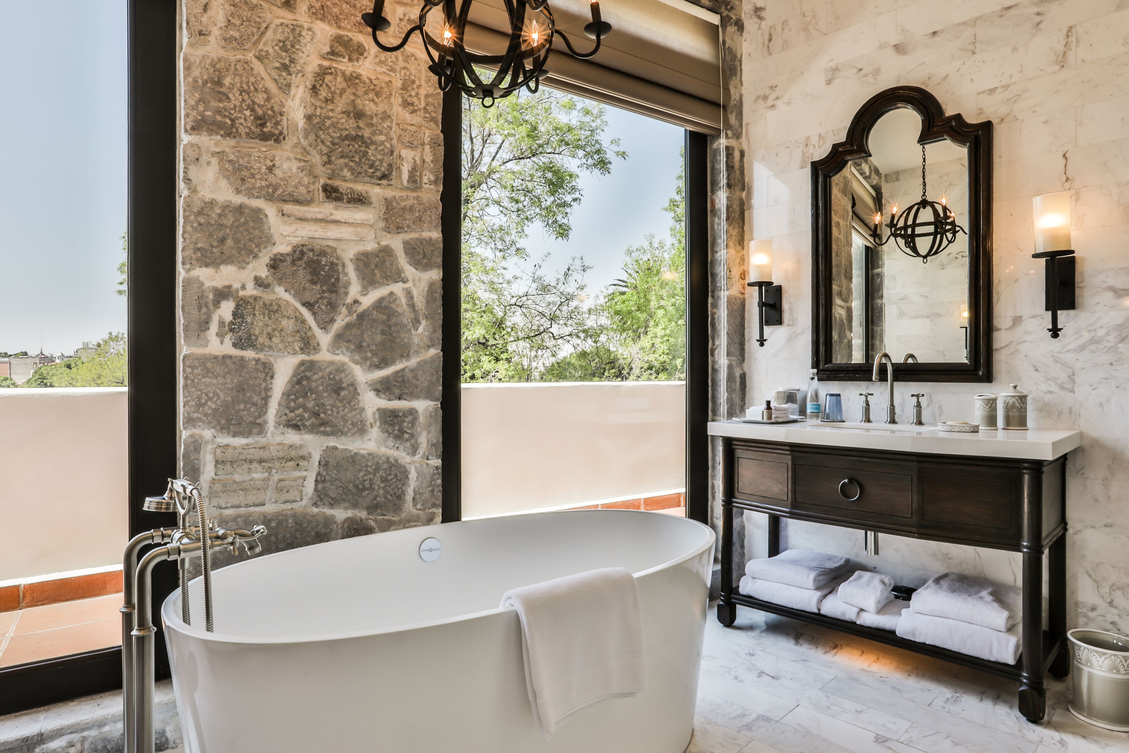A bathroom with a freestanding bathtub, a large mirror, and a stone wall.