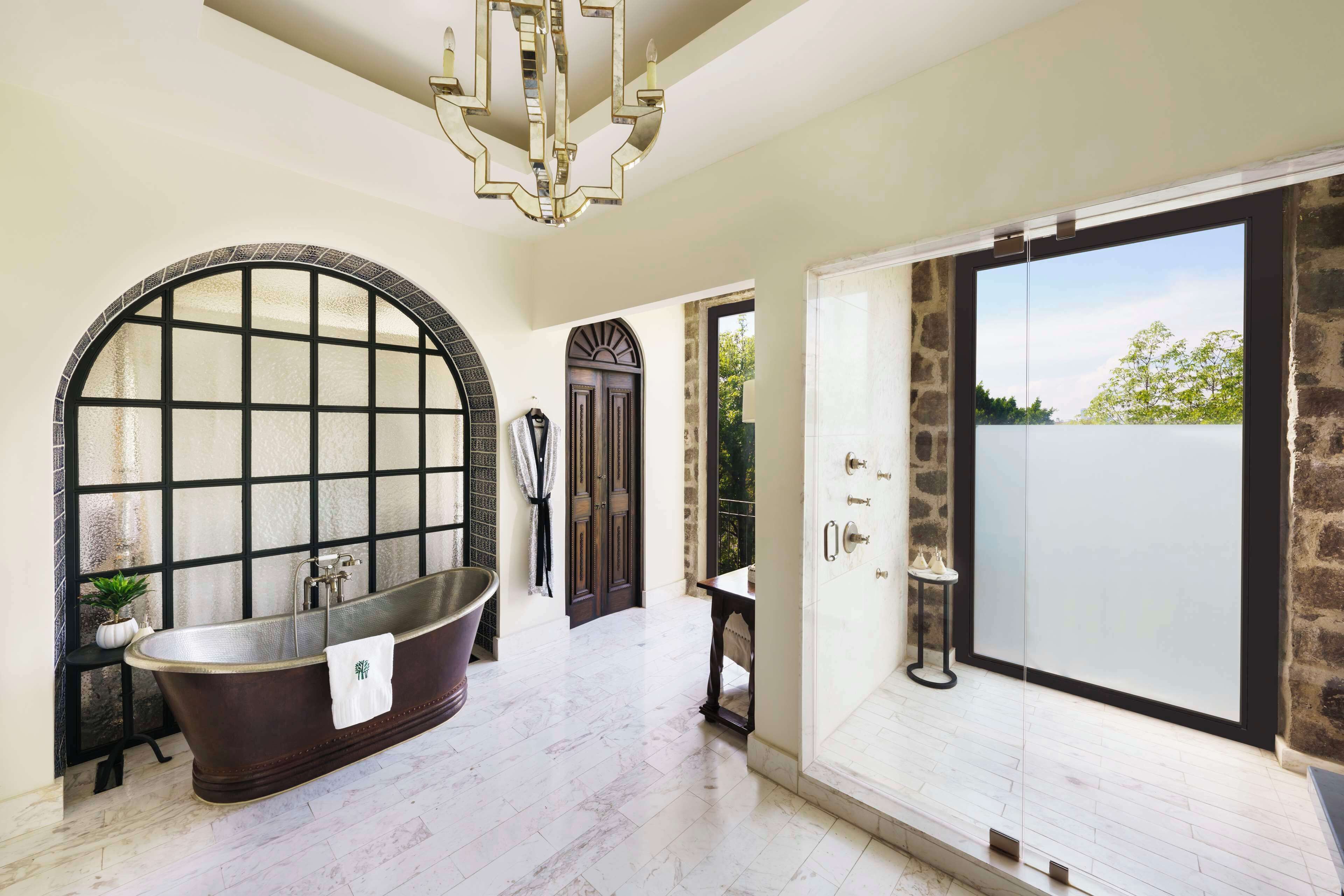 A spacious bathroom with a freestanding bathtub, a large arched window, and a glass-enclosed shower area.