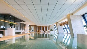 Una piscina interior con diseño moderno, que cuenta con agua cristalina, zonas de estar y ventanas amplias.