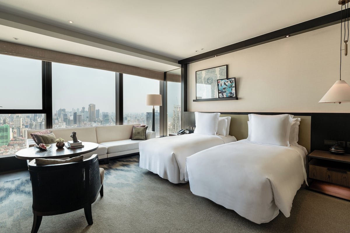 Une chambre d’hôtel avec deux lits, un canapé, une table basse ronde et une vue sur la ville.