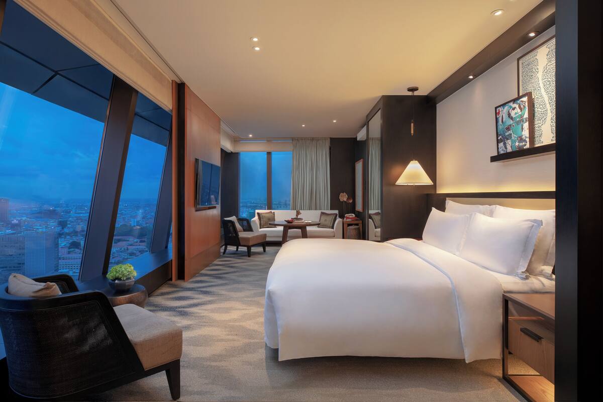 Une chambre d’hôtel avec un grand lit, un bureau, une chaise, une petite table et une vue sur la ville.