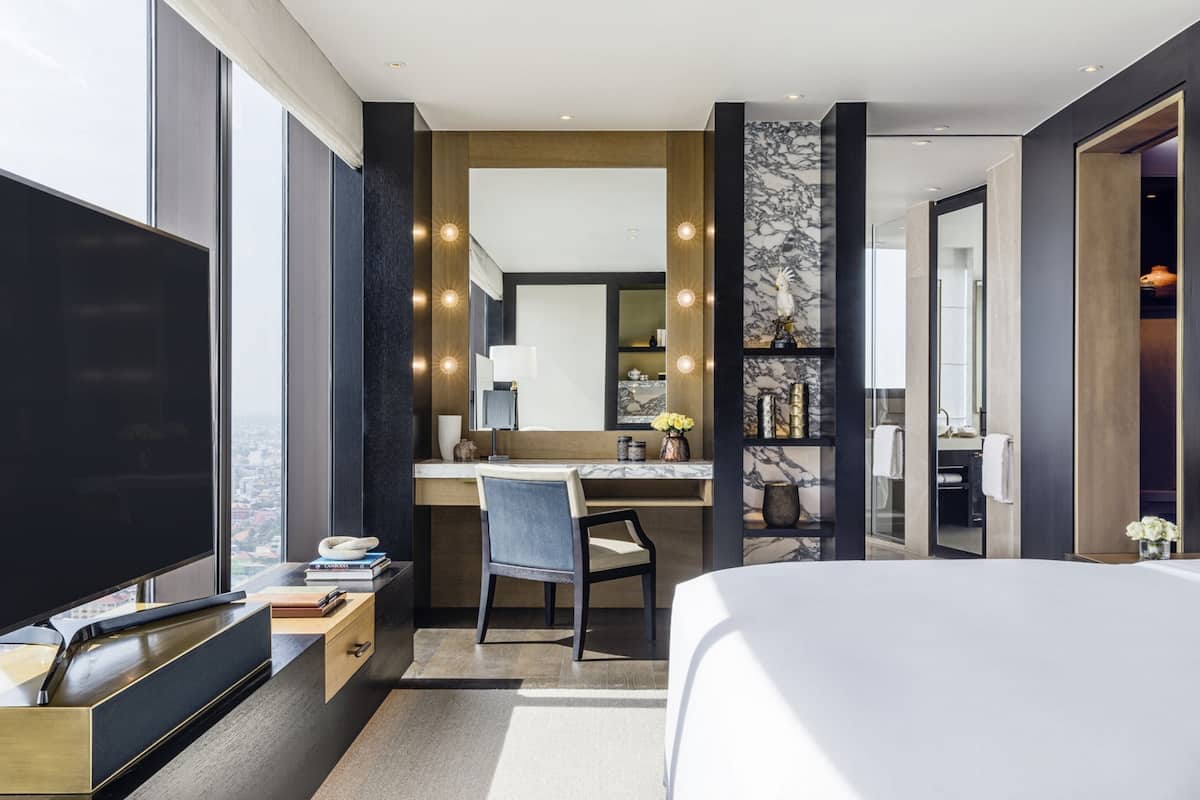 Une chambre d’hôtel moderne, dotée d’un grand lit, d’un bureau avec une chaise, d’une télévision et d’une salle de bain visible à travers une porte ouverte.