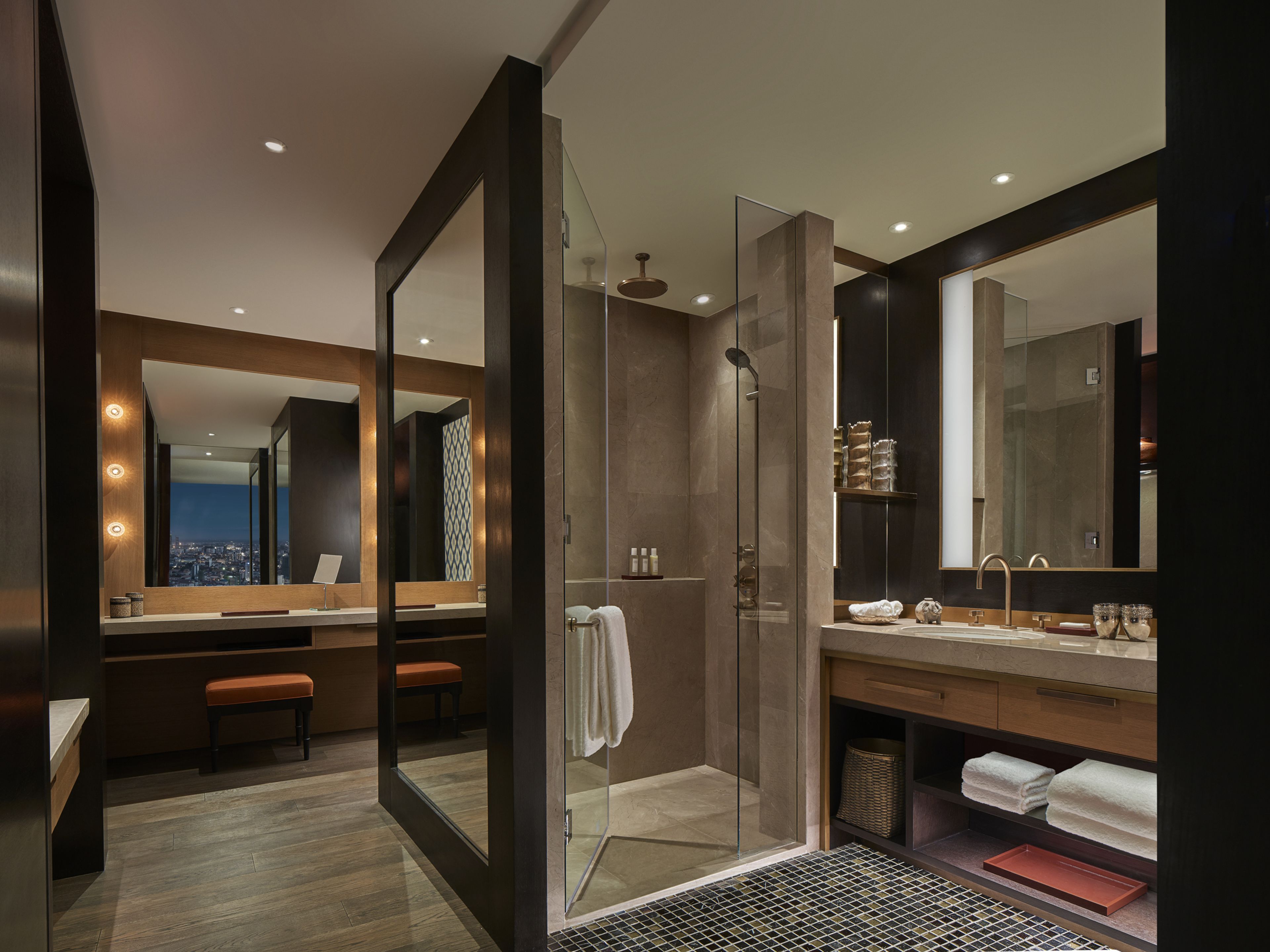 A modern bathroom with a glass-enclosed shower, a vanity with a large mirror, and a bench.