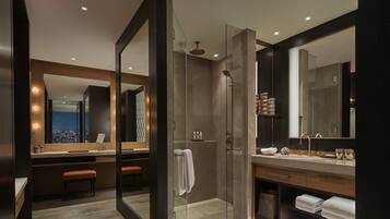A modern bathroom with a glass-enclosed shower, a vanity with a large mirror, and a bench.