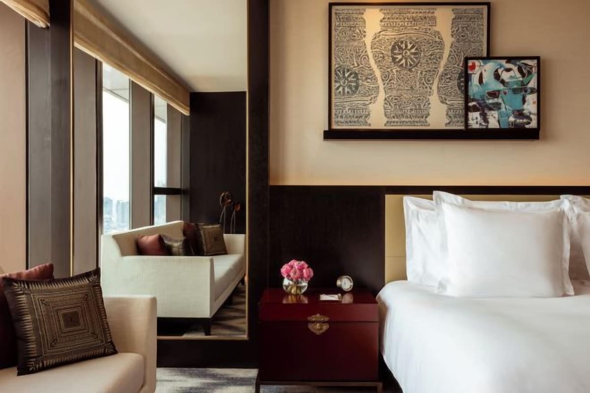 A hotel room with a bed, a nightstand with a vase of flowers, a sofa, and a large wall art piece.