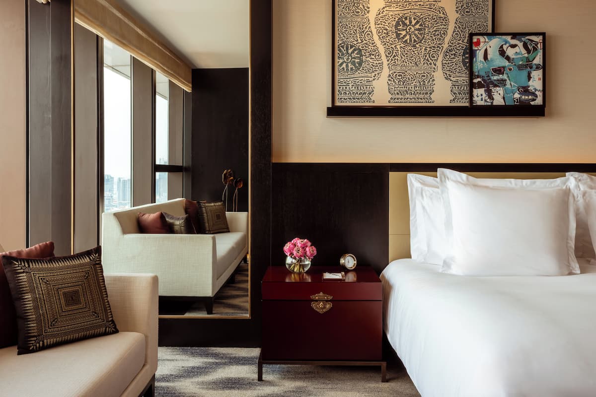 Une chambre d’hôtel comprenant un lit, une table de chevet, un canapé et une grande fenêtre donnant sur la ville.