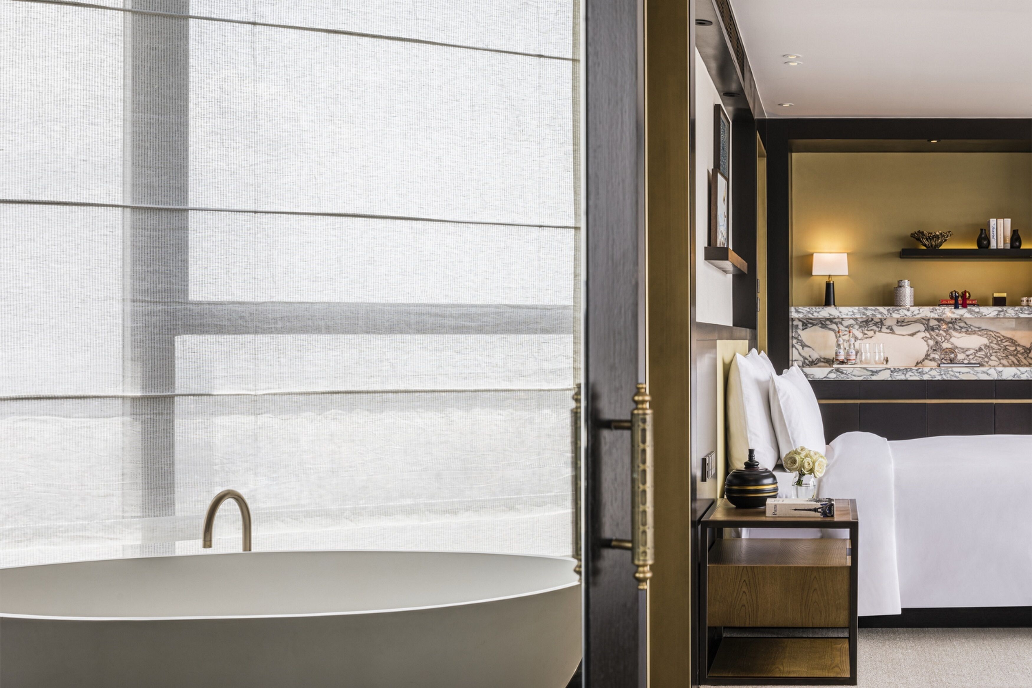 Un baño moderno con una bañera independiente, encimera de mármol y mesita de noche con lámpara y objetos decorativos.