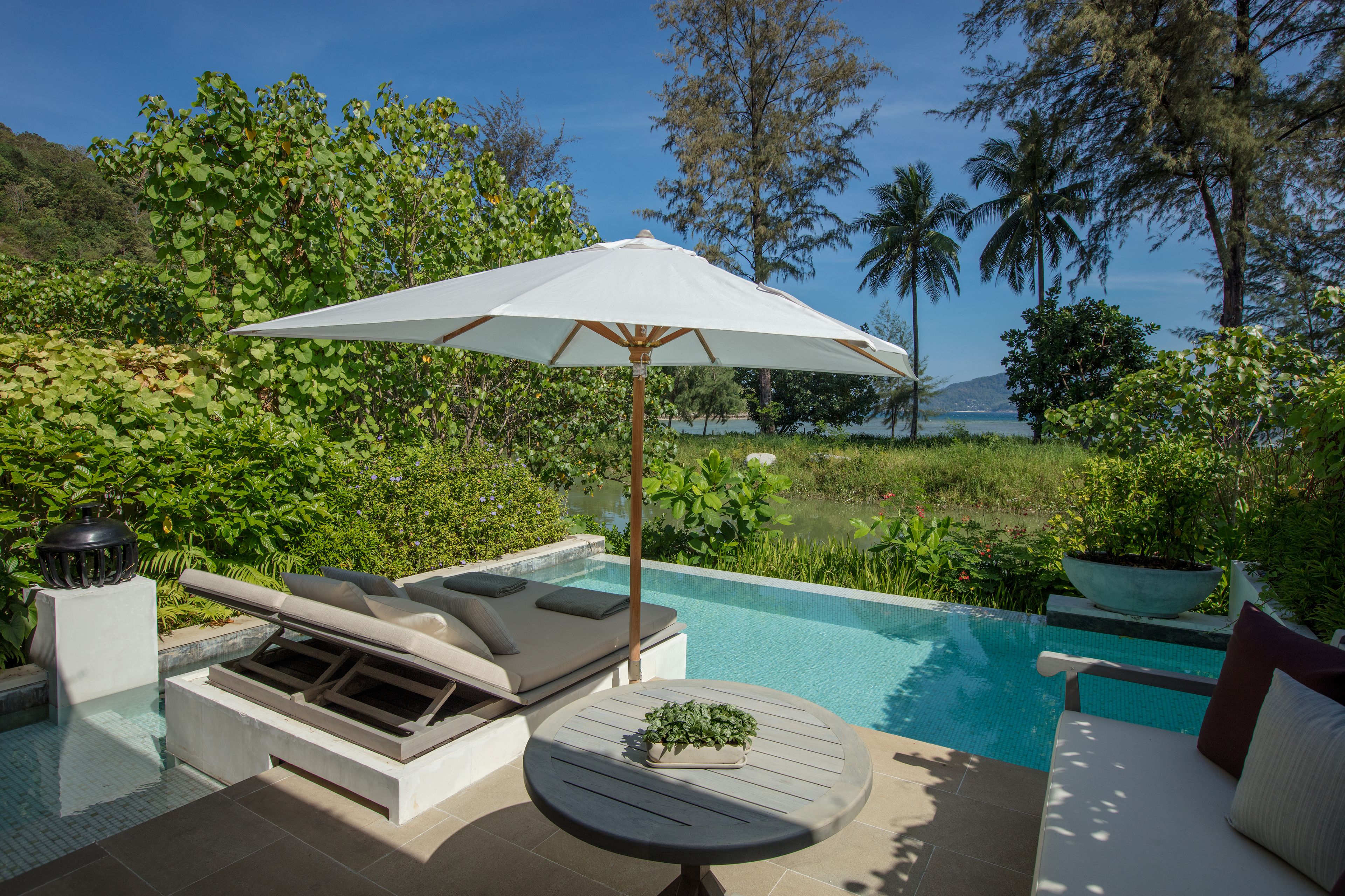 A poolside area with a lounge chair, a table with a plant, and a large umbrella.