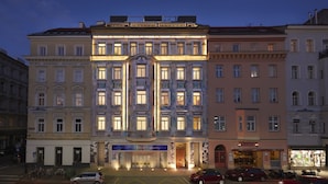 Um edifício de vários andares com entrada central, grandes janelas e espaço comercial no térreo.