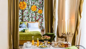 Quarto de hotel com cama, mesa de café da manhã com comida e bebida, e parede decorada com motivos florais.