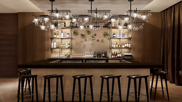 Eine Bar mit einer langen Theke, mehreren Hockern und einer Deckenleuchte mit hängenden Glaskugeln.