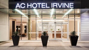 Das moderne Äußere des AC Hotel Irvine mit großem Eingang, Glasüren und zwei Kübelpflanzen im Vordergrund.