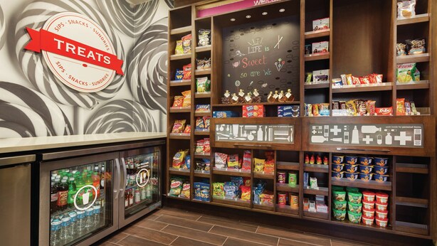 A snack display with various packaged goods and a refrigerator with beverages. - Hampton Inn St. Albans (St. Albans)