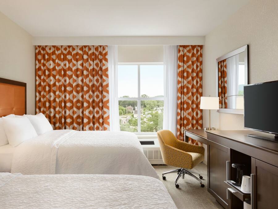 Une chambre d’hôtel avec deux lits, un bureau, une chaise, une télévision et une fenêtre avec des rideaux.
