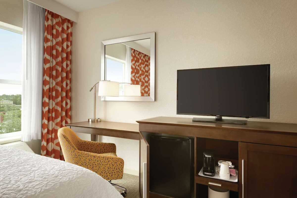 A hotel room with a bed, a desk with a television, a chair, and a coffee maker.