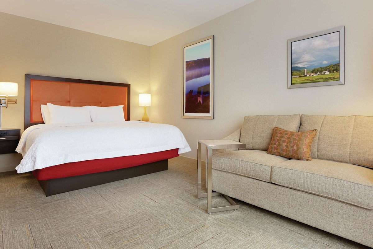 A hotel room with a bed, a sofa, two wall-mounted lamps, and two framed pictures.