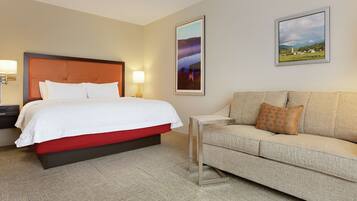 A hotel room with a bed, a sofa, two wall-mounted lamps, and two framed pictures.
