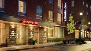 A hotel with a stone facade, large windows, and a neon sign. - Hampton Inn St. Albans (St. Albans)