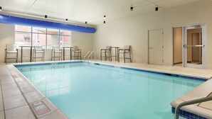 A swimming pool with clear blue water, surrounded by white tiled walls and a blue ceiling. There are chairs and a door visible in the background. - Hampton Inn St. Albans (St. Albans)