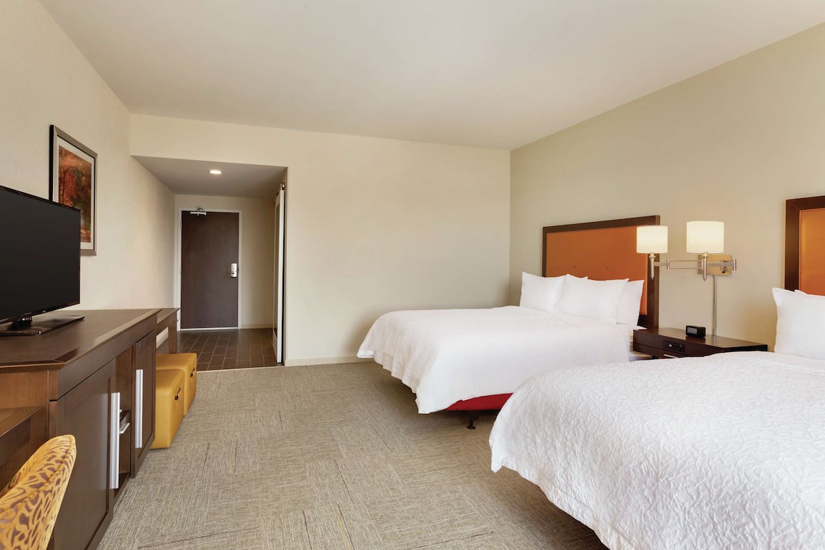A hotel room with two beds, a TV on a wooden dresser, and a lamp on the nightstand.