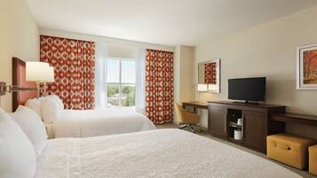A hotel room with two beds, a TV, a desk, and a window with curtains.