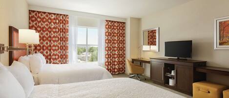 A hotel room with two beds, a TV, a desk, and a window with curtains.