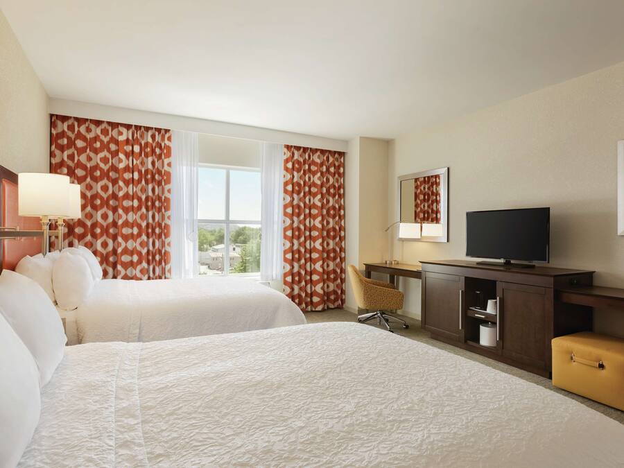 A hotel room with two beds, a TV, a desk, and a window with curtains.