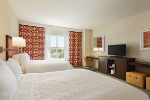 A hotel room with two beds, a TV, a desk, and a window with curtains.