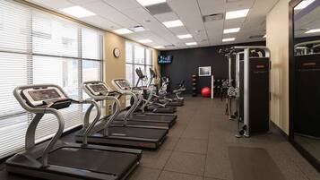 A gym with treadmills, weight machines, and a TV screen.