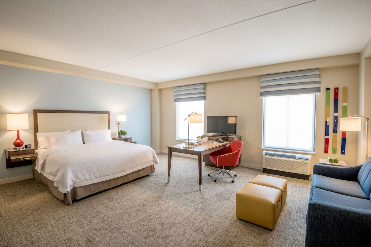 Ett hotellrum med en stor säng, ett skrivbord med en stol, en soffa och en tv.