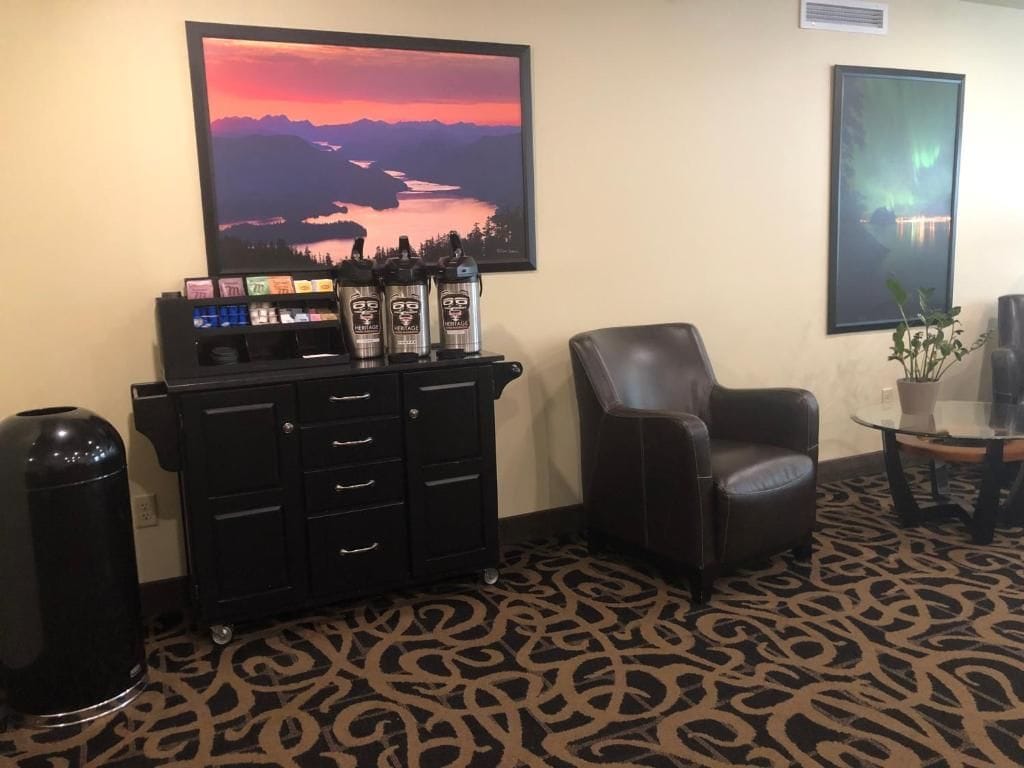 Une pièce comprenant un meuble noir, un fauteuil en cuir et un grand tableau encadré représentant un coucher de soleil sur des montagnes.
