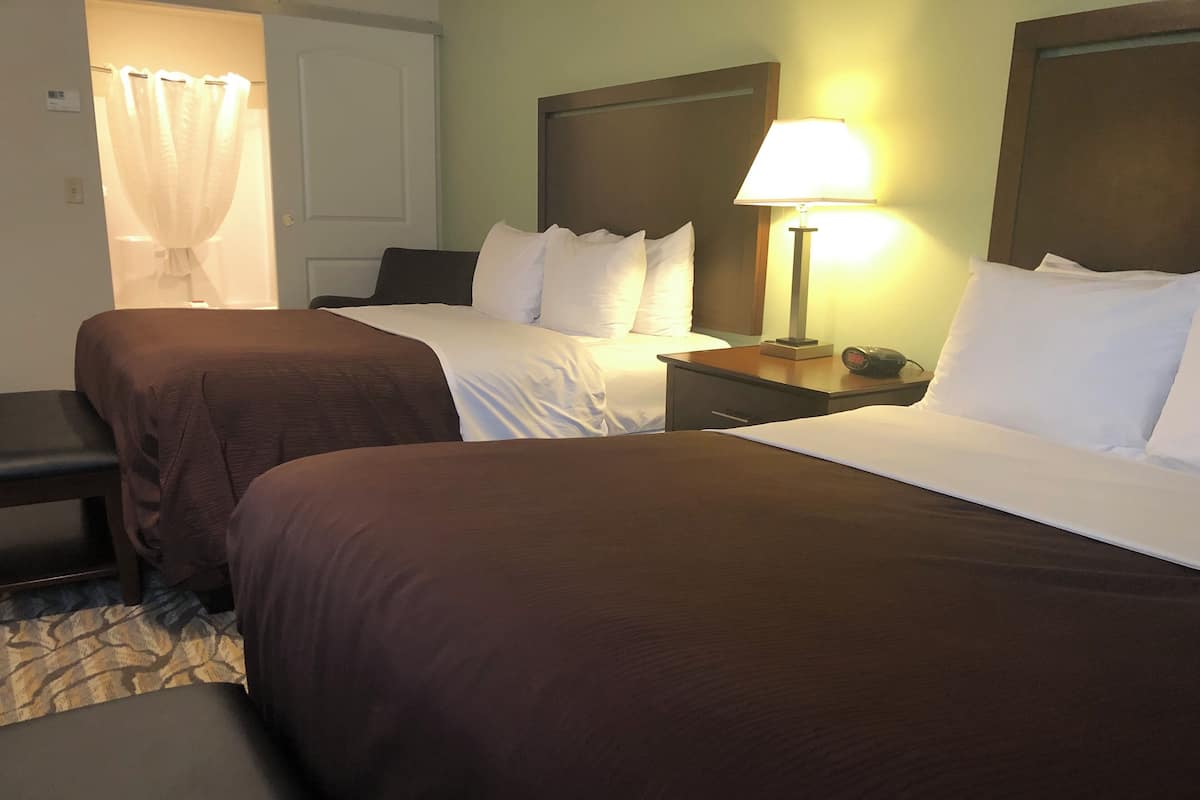 A hotel room with two beds, a nightstand with a lamp, a chair, and a curtain.