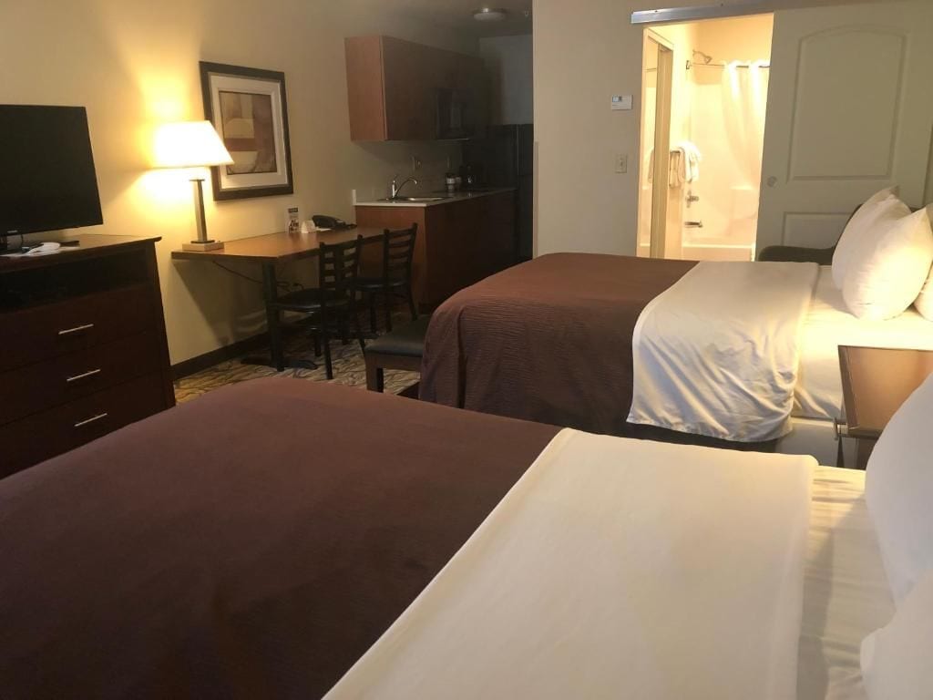 A hotel room with two beds, a desk, a chair, a television, and a kitchenette.