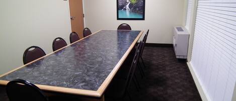 A conference room with a long table, chairs, a door, a framed picture of a waterfall, and an air conditioning unit.