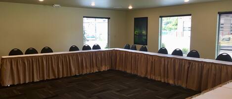 Un salón de conferencias con una larga mesa, múltiples sillas y ventanas amplias.