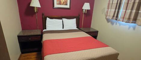 A hotel room with a bed, two bedside tables, a lamp, a painting on the wall, and a window with curtains.