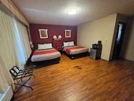 A hotel room with two beds, a desk, a chair, a microwave, and a door leading to another room.
