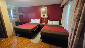 A hotel room with two beds, a wooden floor, a mirror, a nightstand, and a window with curtains.