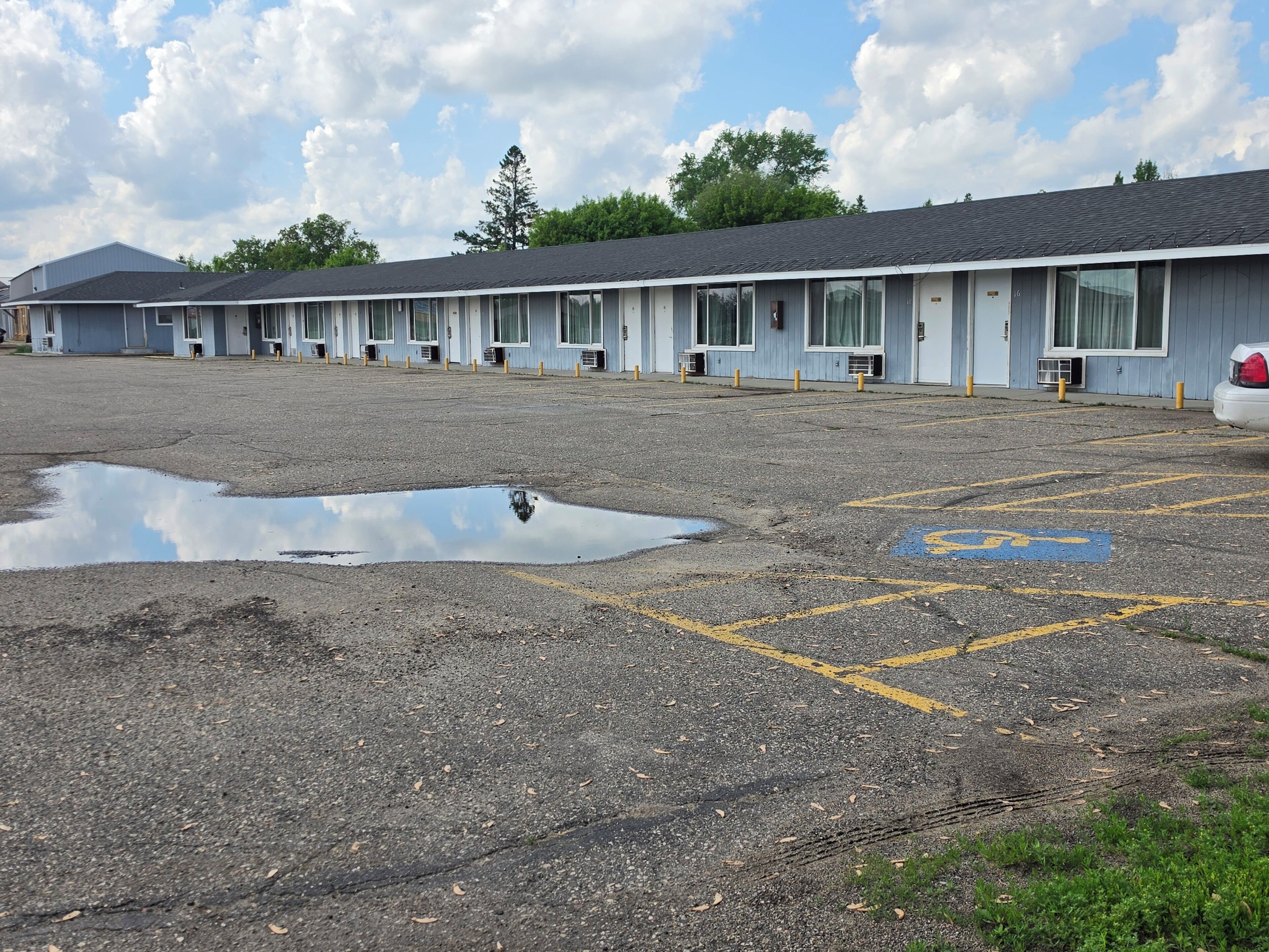 A motel with a row of rooms, a parking lot with a visible handicap parking space, and a large puddle on the ground.